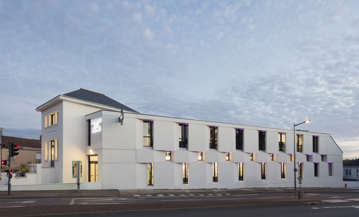 La construction de cette pharmacie s’implante en coeur de ville sur une parcelle très en pente. L’implantation reprend les limites de la parcelle et le dénivelé permet de créer deux niveaux de parkings. Les façades sont travaillées de manière à donner un rythme et une épaisseur compensant le peu d’ouvertures. Enfin des éléments d’architecture du bâtiment des bains douches choletais présents sur la parcelle sont récupérés et remis en scène à l’entrée de la pharmacie.